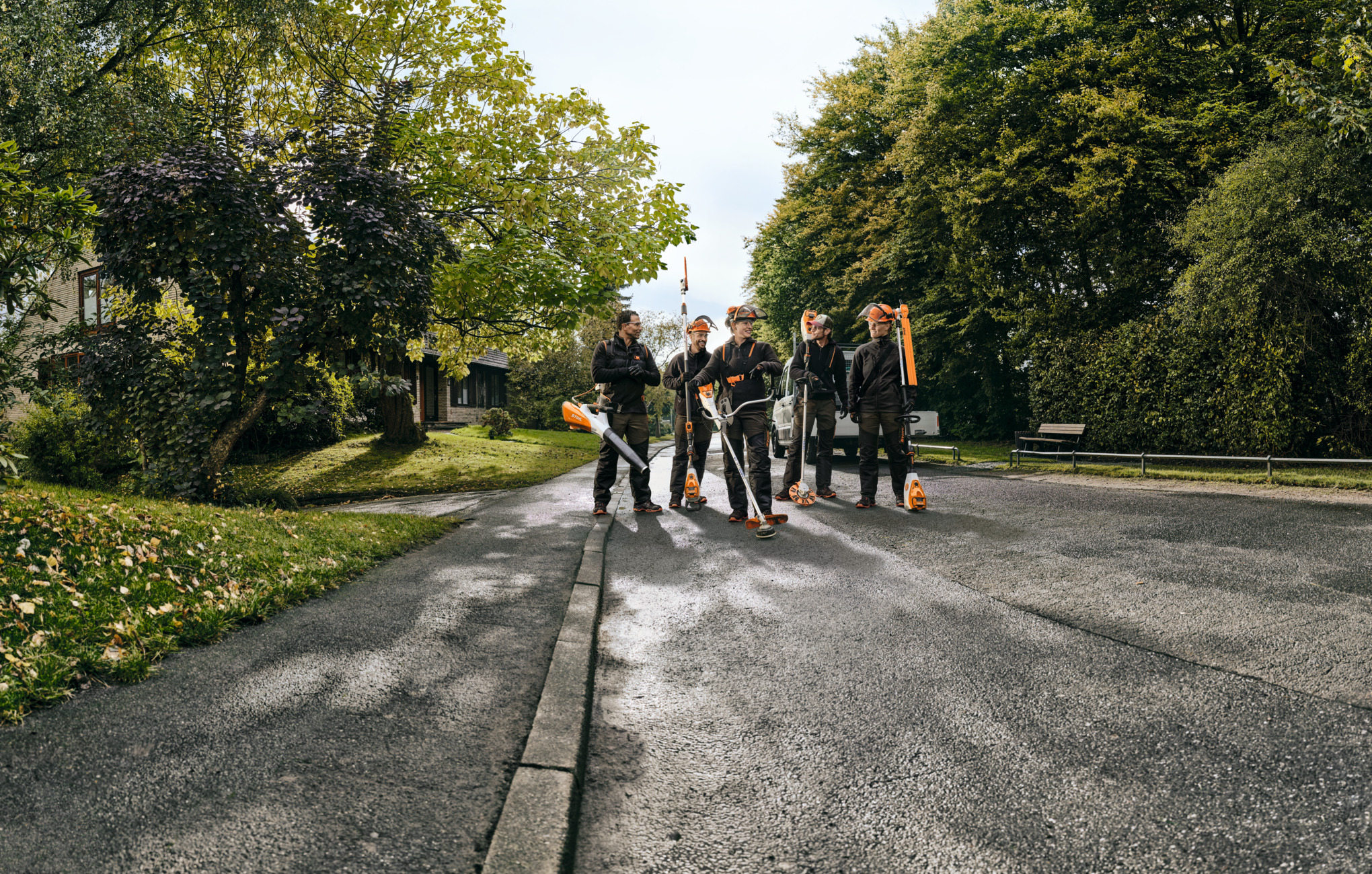 Viisi STIHL-ammattilaista kävelemässä tien varrella akkutyökalujen kanssa
