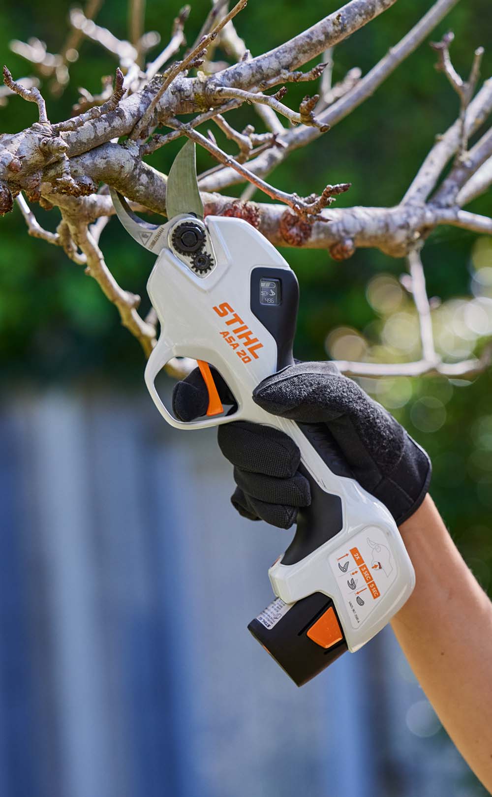 En kvinna med ansiktsskydd klipper gräs med STIHL FSA 45 batteridriven grästrimmer runt ett trappsteg framför ett hus