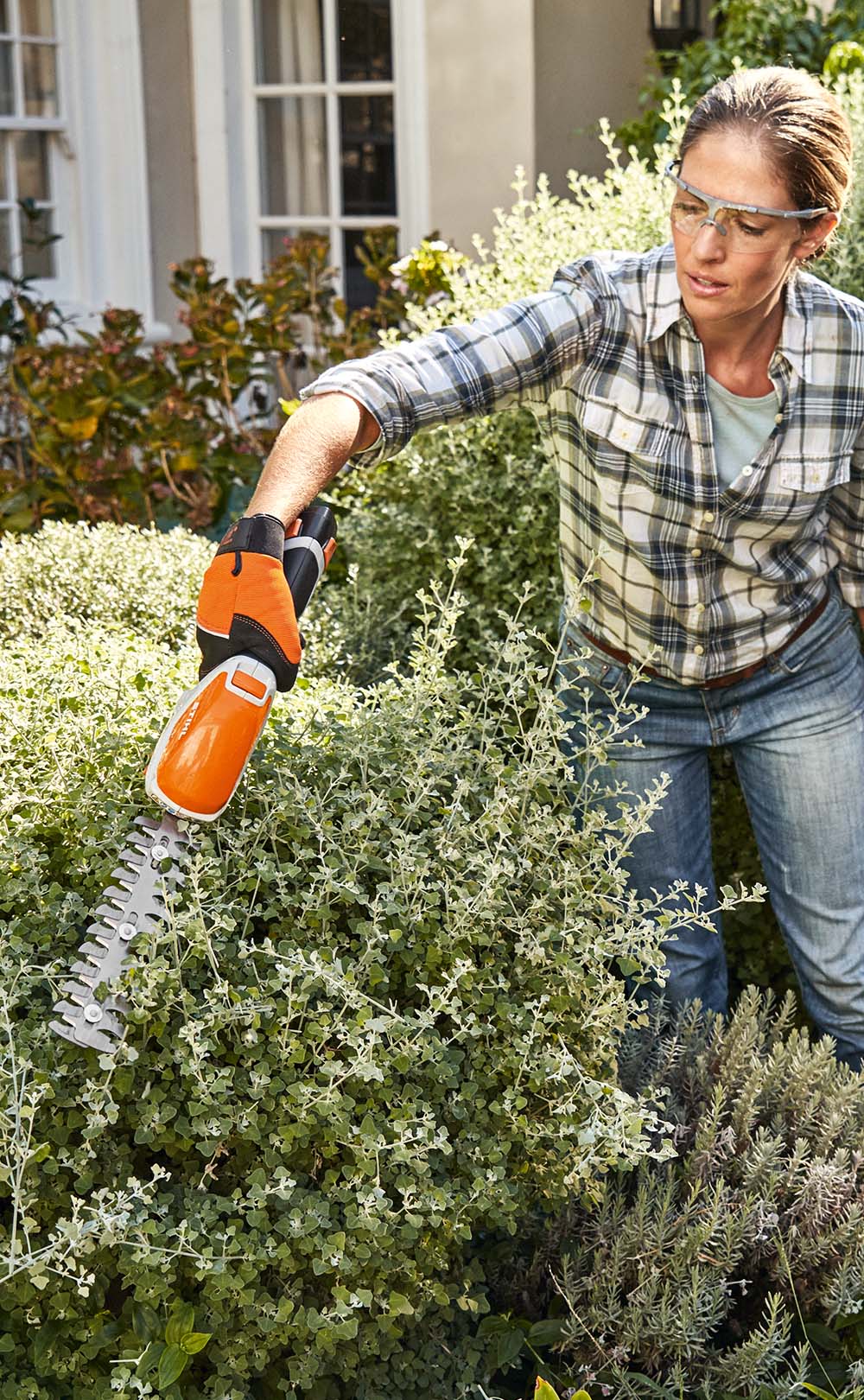 En kvinna med ansiktsskydd klipper gräs med STIHL FSA 45 batteridriven grästrimmer runt ett trappsteg framför ett hus